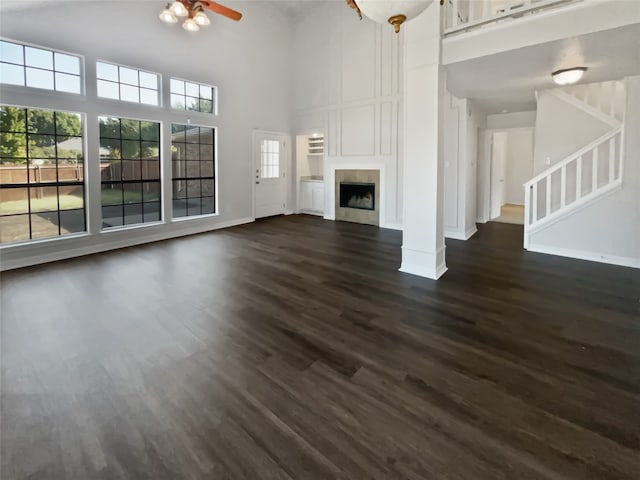 unfurnished living room with ceiling fan, a towering ceiling, and dark hardwood / wood-style flooring