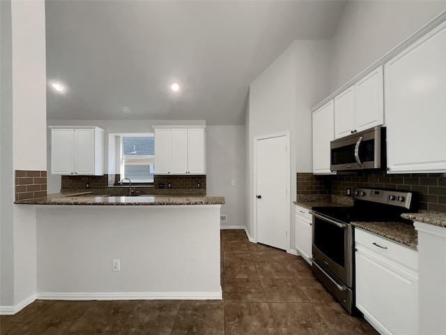 kitchen with stainless steel appliances, dark stone counters, white cabinets, and a peninsula