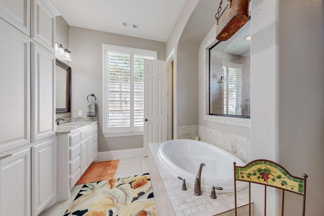 bathroom with tile patterned flooring, tiled bath, and vanity