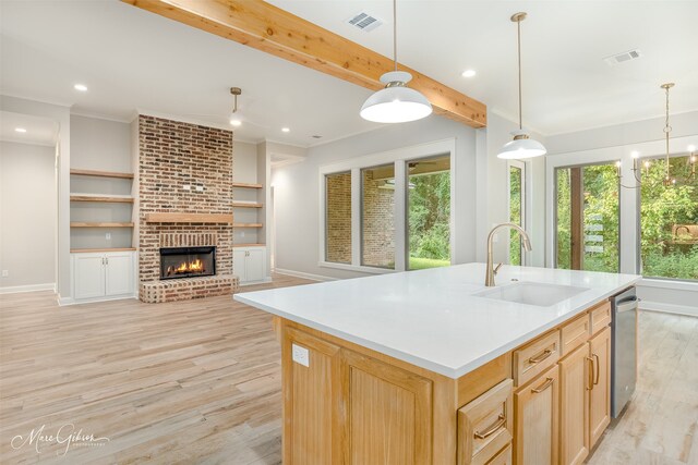 kitchen featuring sink, light brown cabinets, a brick fireplace, beamed ceiling, and a kitchen island with sink