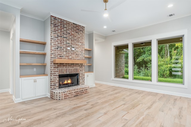 unfurnished living room with crown molding, a brick fireplace, ceiling fan, built in features, and light hardwood / wood-style floors