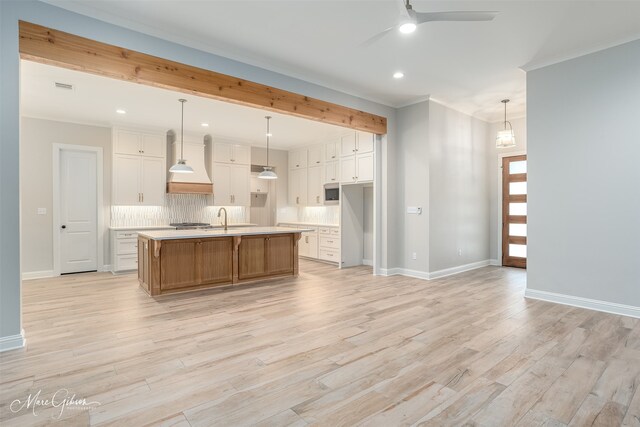 kitchen featuring a sink, custom range hood, light countertops, light wood finished floors, and tasteful backsplash