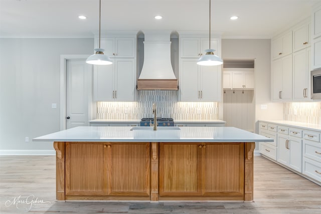 kitchen with white cabinetry, sink, light hardwood / wood-style flooring, a kitchen island with sink, and custom range hood