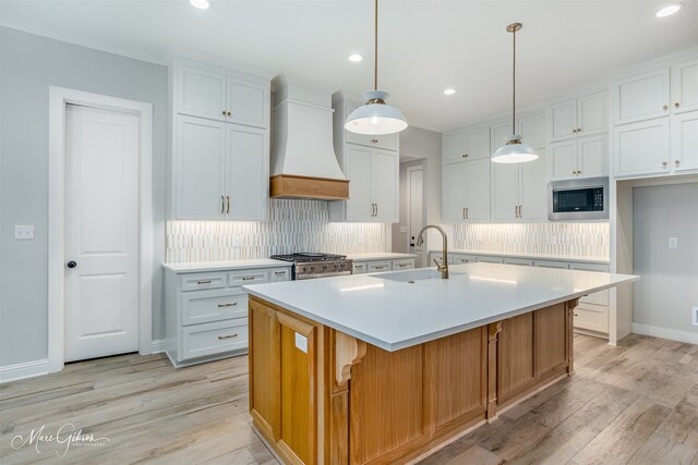 kitchen featuring premium range hood, a kitchen island with sink, built in microwave, sink, and white cabinets