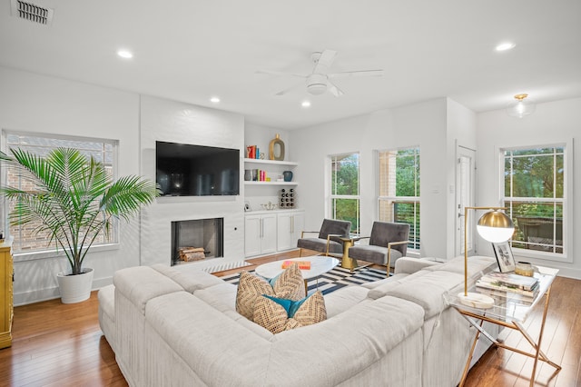 living room featuring a healthy amount of sunlight, hardwood / wood-style floors, ceiling fan, and a large fireplace