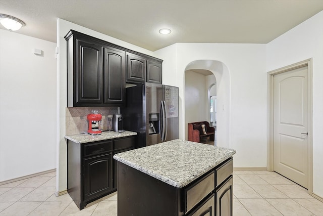 kitchen with tasteful backsplash, light tile patterned floors, light stone countertops, stainless steel refrigerator with ice dispenser, and a center island