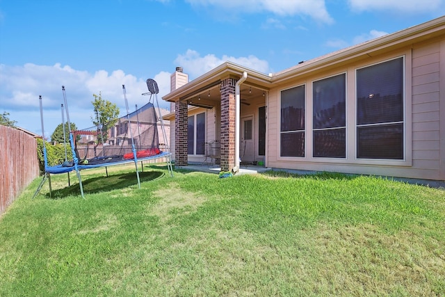 rear view of property featuring a trampoline and a lawn