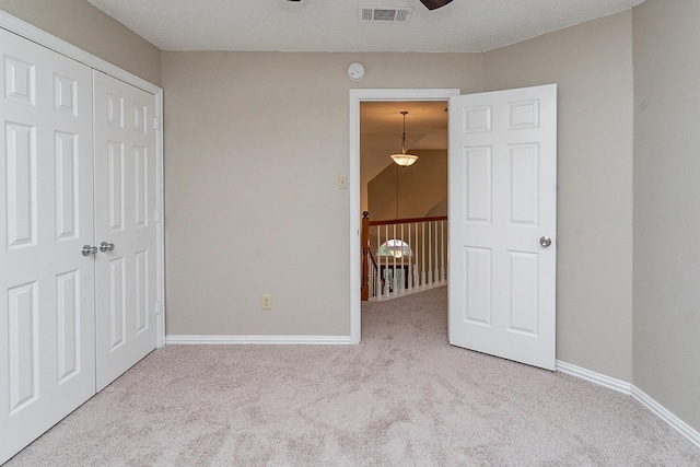 unfurnished bedroom with a textured ceiling, light colored carpet, and a closet