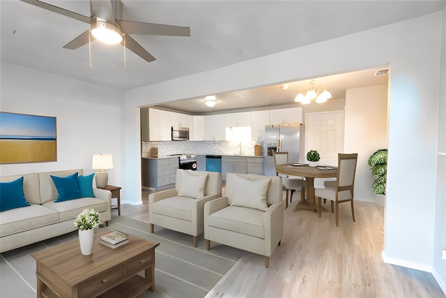 living room with ceiling fan with notable chandelier, sink, and light hardwood / wood-style flooring