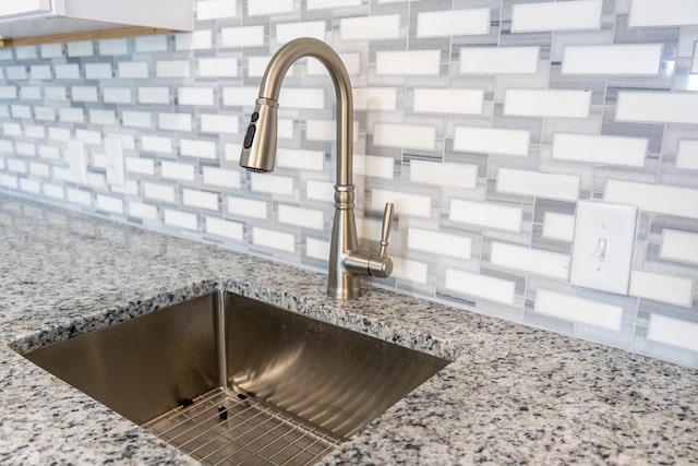 details featuring light stone countertops, sink, and tasteful backsplash