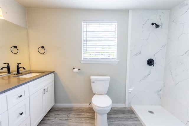 bathroom featuring wood-type flooring, tiled shower, vanity, and toilet