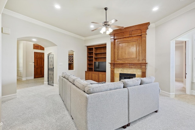 carpeted living room with crown molding, built in shelves, ceiling fan, and a large fireplace