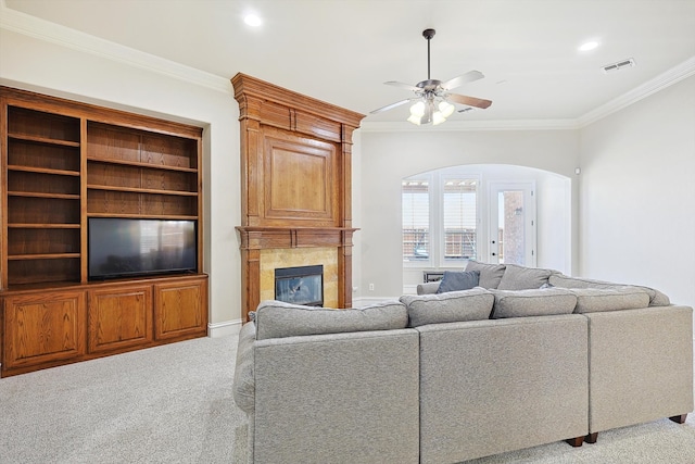 living room with crown molding, light colored carpet, ceiling fan, and a tile fireplace