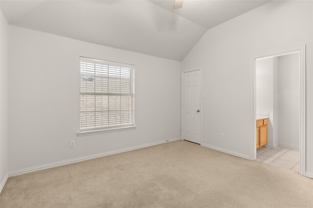 unfurnished bedroom with lofted ceiling, ceiling fan, light carpet, and ensuite bathroom