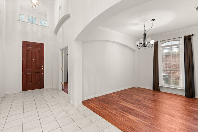 entryway with crown molding, a wealth of natural light, light tile patterned floors, and a notable chandelier