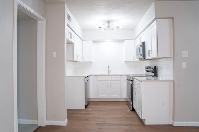 kitchen with hardwood / wood-style floors, backsplash, sink, appliances with stainless steel finishes, and white cabinets