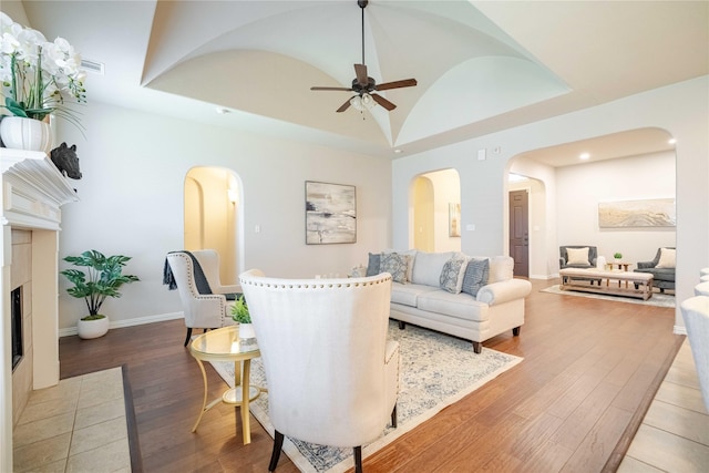 living area with a fireplace with flush hearth, arched walkways, a raised ceiling, and wood finished floors