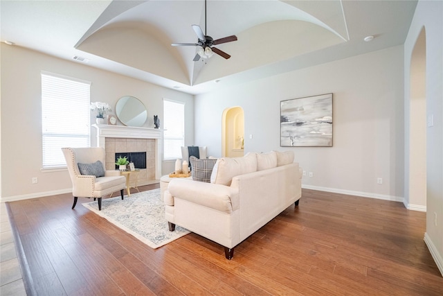 living room with plenty of natural light, wood-type flooring, a raised ceiling, and a tiled fireplace