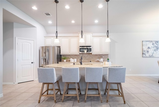 kitchen featuring a breakfast bar, a sink, appliances with stainless steel finishes, backsplash, and a center island with sink