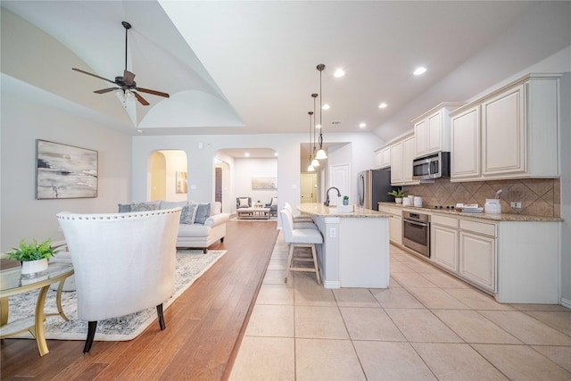 kitchen with tasteful backsplash, arched walkways, appliances with stainless steel finishes, a breakfast bar, and open floor plan