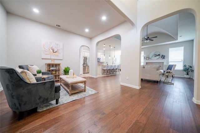 living room featuring baseboards, visible vents, a ceiling fan, arched walkways, and dark wood-style flooring