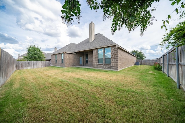 rear view of house featuring a yard, brick siding, a chimney, and a fenced backyard