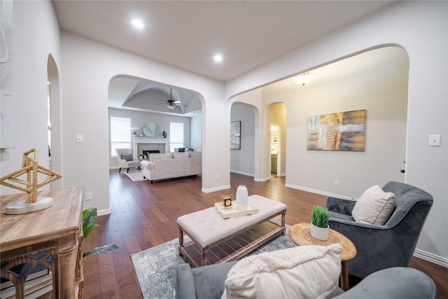 living area with arched walkways, ceiling fan, wood finished floors, baseboards, and a tiled fireplace