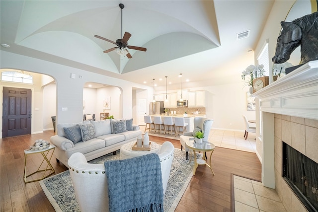 living room featuring light wood finished floors, baseboards, visible vents, arched walkways, and a tile fireplace