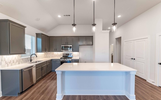 kitchen with a center island, sink, hanging light fixtures, vaulted ceiling, and appliances with stainless steel finishes