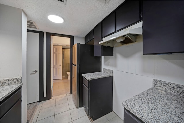 kitchen featuring stainless steel fridge, light tile patterned floors, and a textured ceiling