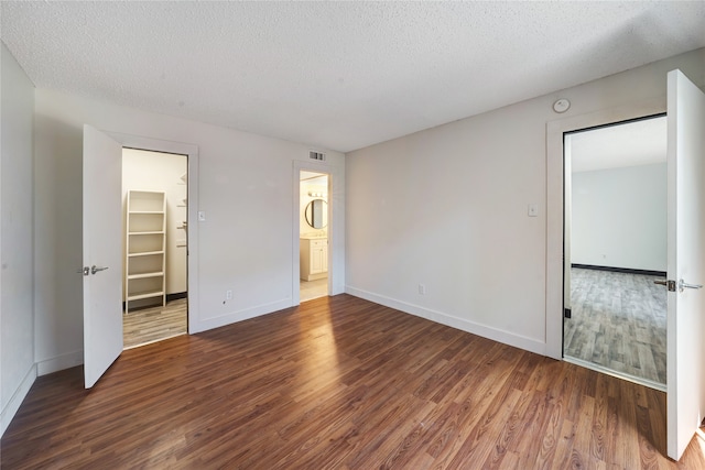 unfurnished bedroom featuring a textured ceiling, connected bathroom, dark hardwood / wood-style flooring, a closet, and a walk in closet