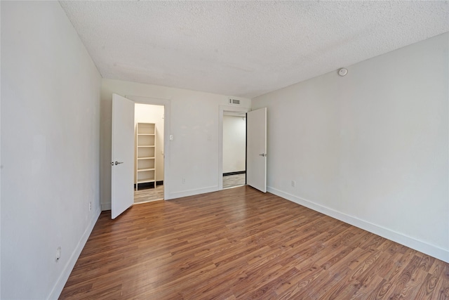 unfurnished bedroom featuring a textured ceiling, hardwood / wood-style flooring, a spacious closet, and a closet