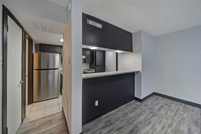 kitchen with a textured ceiling, light hardwood / wood-style flooring, and stainless steel refrigerator