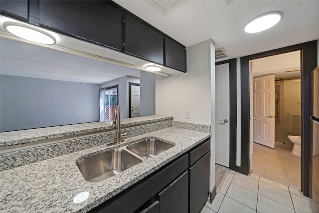 kitchen with a textured ceiling, light stone countertops, sink, and light tile patterned flooring