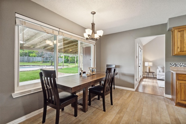 dining room featuring a textured ceiling, baseboards, light wood-style flooring, and a notable chandelier