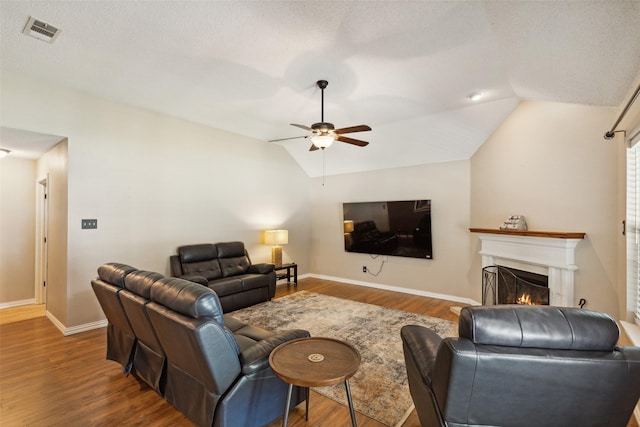 living room with lofted ceiling, visible vents, a ceiling fan, wood finished floors, and a lit fireplace