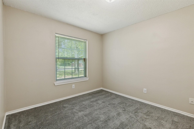 empty room featuring a textured ceiling, dark colored carpet, and baseboards