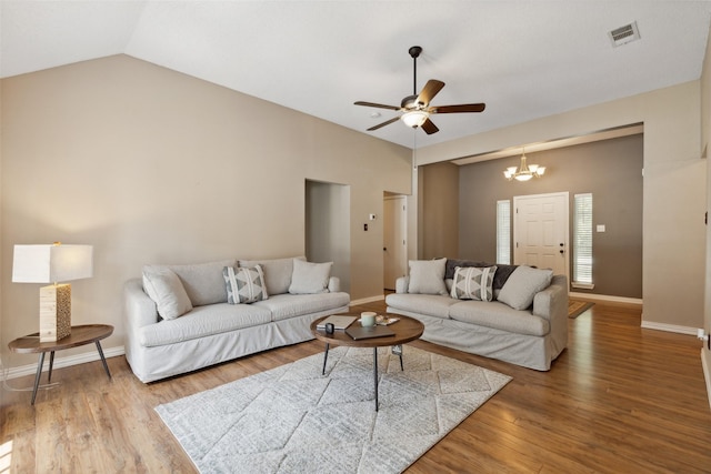 living area featuring lofted ceiling, visible vents, wood finished floors, baseboards, and ceiling fan with notable chandelier