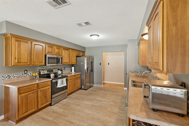 kitchen with appliances with stainless steel finishes, a textured ceiling, sink, and light hardwood / wood-style floors