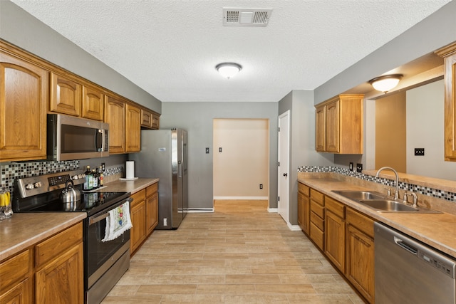 kitchen with tasteful backsplash, a textured ceiling, sink, appliances with stainless steel finishes, and light hardwood / wood-style floors