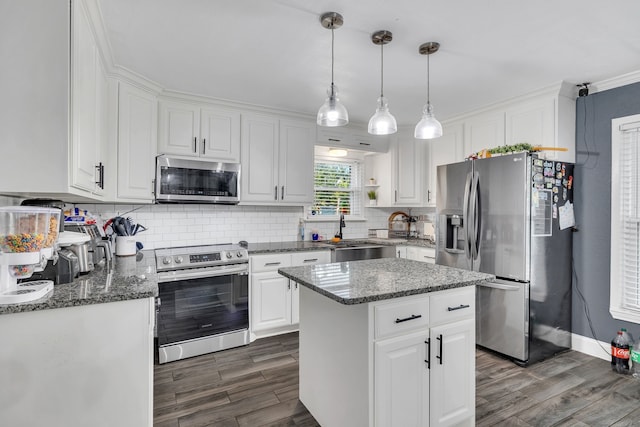 kitchen with appliances with stainless steel finishes, pendant lighting, sink, white cabinets, and a center island