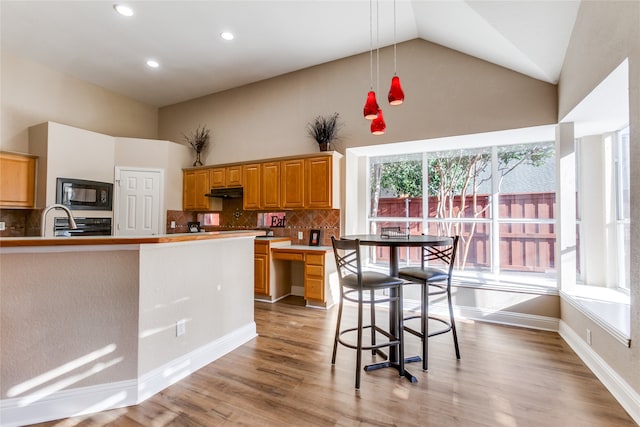 kitchen featuring backsplash, light wood-type flooring, black microwave, high vaulted ceiling, and pendant lighting