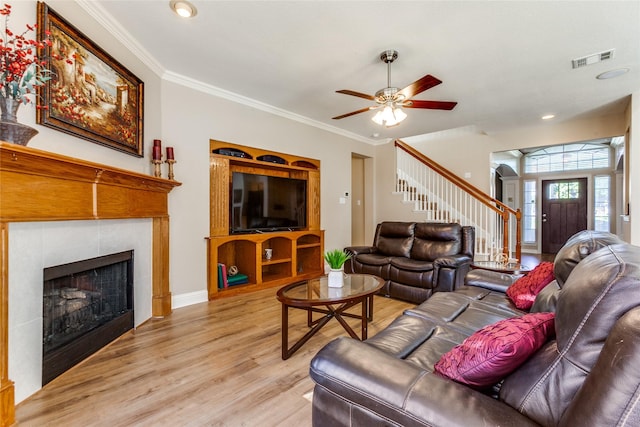 living room with ornamental molding, light wood-style flooring, a tiled fireplace, and visible vents