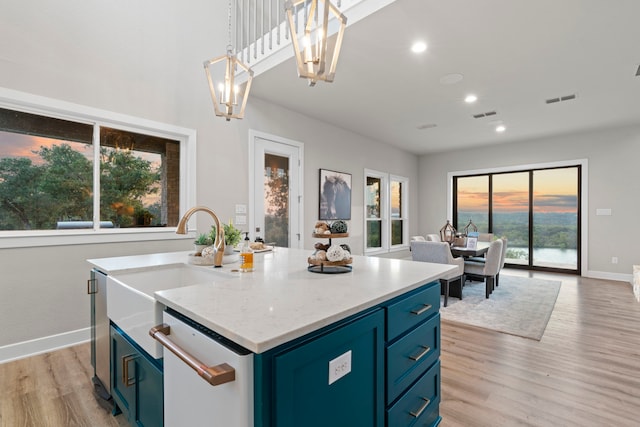 kitchen featuring a kitchen island with sink, dishwasher, decorative light fixtures, and blue cabinets