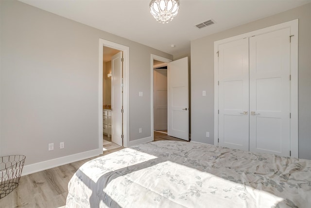 bedroom featuring connected bathroom, a closet, a chandelier, and light wood-type flooring