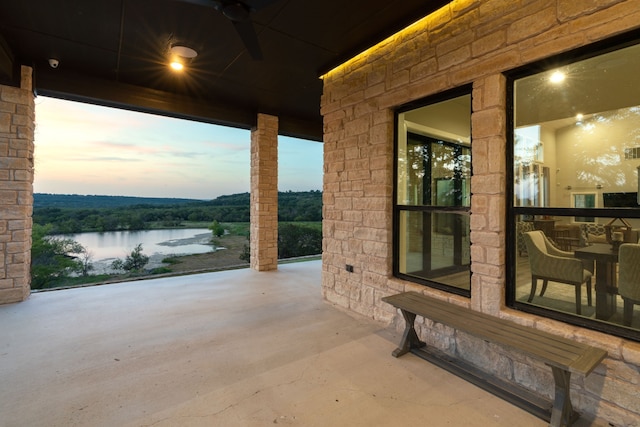 patio terrace at dusk featuring ceiling fan and a water view