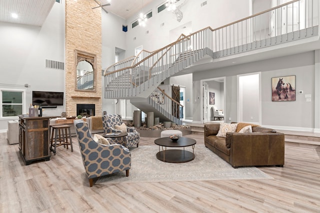 living room with ceiling fan, light hardwood / wood-style floors, a stone fireplace, and a towering ceiling