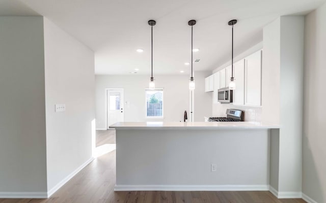 kitchen featuring white cabinetry, sink, kitchen peninsula, decorative light fixtures, and appliances with stainless steel finishes