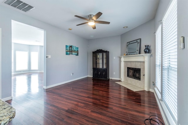 unfurnished living room featuring a tile fireplace, dark hardwood / wood-style flooring, ceiling fan, and a healthy amount of sunlight