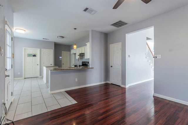 kitchen with kitchen peninsula, stainless steel range, stone countertops, light hardwood / wood-style flooring, and white cabinetry